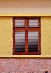 One simple closed window with wooden shutters in a yellow wall.
