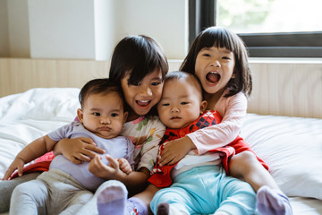 four Asian children laugh while sitting on the bed hugging each other