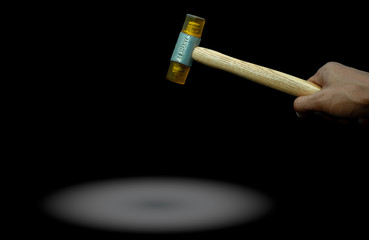 Man's hand holding plastic hammer isolated on dark background. Male worker's hand hold wood handle of plastic hammer. Hammer head made of soft and tough yellow plastic that not damage workpiece.
