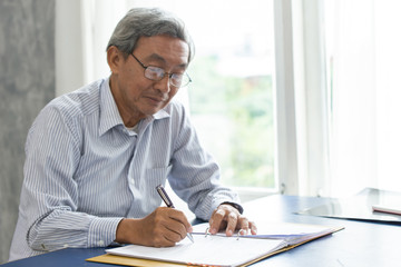 Asian smart business elder writing document report in the office.