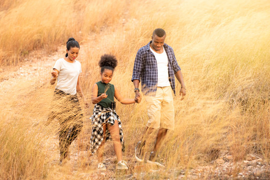 Portrait of Happy young African family father, mother and daughter hiking and holding hands together with smiling face. Relaxing family  parents and child walking together on golden meadow on mountain