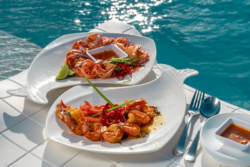 Shrimps starters with orange sauce and lime on white plates, turquoise pool background