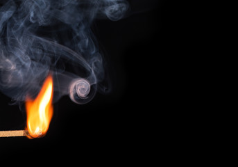 Match bursting into flame with smoke against black background