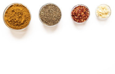 various spices in glass bowls on white background. Top view copy space. Culinary Concept with curry, italina herb mix, crushed pepper and garlic