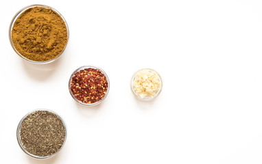 various spices in glass bowls on white background. Top view copy space. Culinary Concept with curry, italina herb mix, crushed pepper and garlic