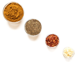 various spices in glass bowls on white background. Top view copy space. Culinary Concept with curry, italina herb mix, crushed pepper and garlic