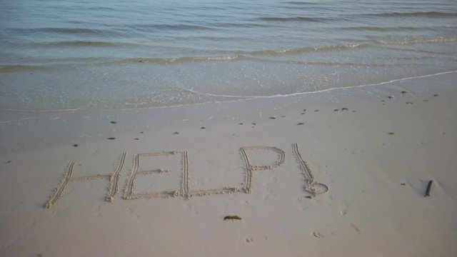 HELP! written in the sand and camera pitches up and turns.