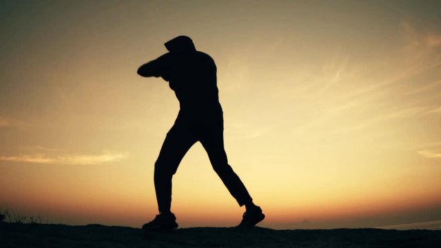 Man practices shadowboxing on a rock by the sea at dawn