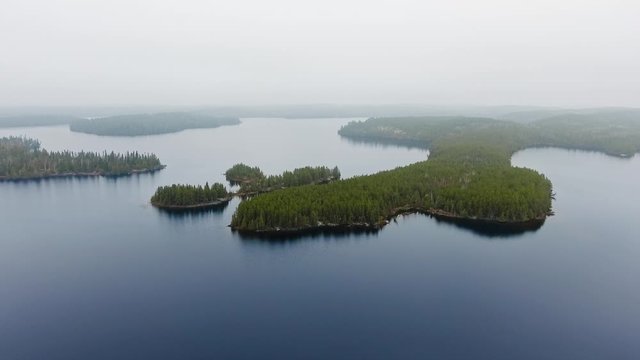 Drone approaching small islands with dense forest in a lake with foggy horizon (Willard Lake, Ontario, Canada)