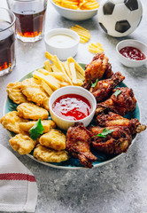 Table fof tasty snacks for beer prepared for watching sports on TV. Chicken. Chicken wings, chicken nuggets, french fries, chips, various sauces and lemonade. Light gray background. Selective focus