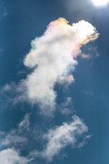 Sun refracting rainbow colors through a white cloud on a sunny blue-sky day