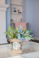 Vintage home decor background, spring flowers in glass vase on a glass table on blurred interior background.Home interior decor in gray and blue colors.Living room decoration.