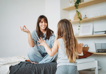 Happy mom and little daughter playing in the bedroom, doing yoga, morning routine