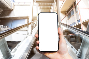 Close-up of female use Hand holding smartphone with empty blank white screen blurred images touch of Abstract blur of mechanical escalator for people going up and down, modern escalators in mall
