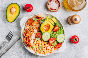 Healthy vegetable buddha bowl lunch with grilled chicken and chickpeas, cucumber, tomato and avocado on light gray background. Top view. Zero waste concept