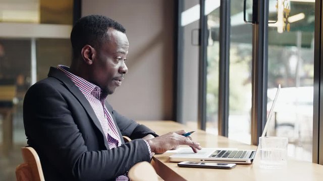 Slow motion of African businessman using laptop in the cafe office by the window getting surprise great good news feel so happy thumb up to the computer screen video meeting online
