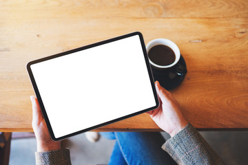 Top view mockup image of a woman holding black tablet pc with blank white screen with coffee cup on the table