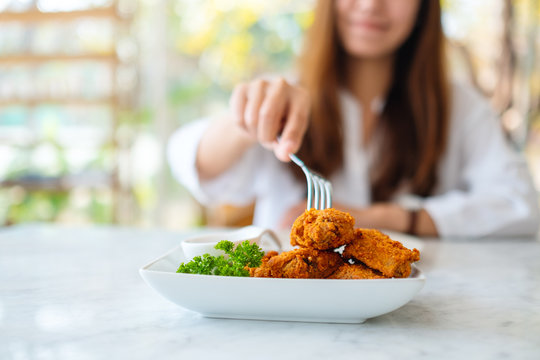 Closeup image of a woman using fork to eat fried chicken in restaurant