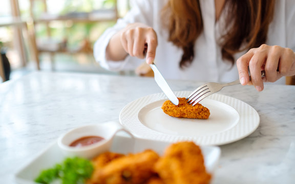 Closeup image of a woman using knife and fork to eat fried chicken in restaurant