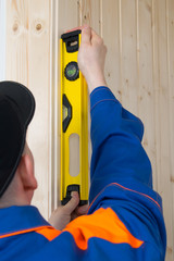 close-up of a level for leveling a wooden surface in the hands of a worker in a blue uniform and a black cap
