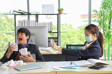 Female employee wearing medical face mask and spraying alcohol spray to her male colleague who is coughing and sneezing for virus and germs prevention
