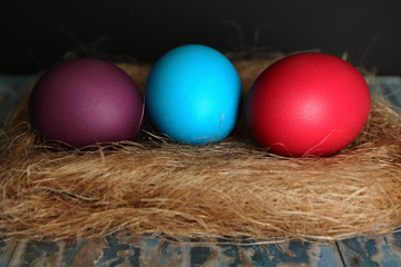 three Easter colored eggs lying on the hay in baskets