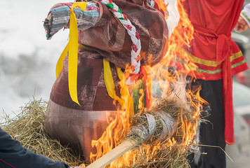 a burning stick with straw that sets fire to a female effigy at the winter festival of spring against the background of a man in a traditional national costume