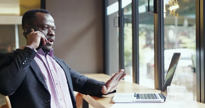 Unhappy African businessman talking on the phone say no disagree business communication problem negotiation on the phone in the office