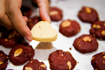 A hand hold a love shape cookies in the middle of red velvet cookies on a tray