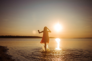 Silhouette of a girl running on water against the background of an evening sunset. Water splashes in all directions. Carefree happy baby fun.