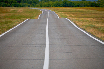 Road in a field on a summer day. Asphalt road for cars in the field.