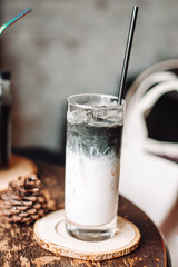 Ice charcoal latte on a wood table with cream being poured into it showing the texture and refreshing look of the drink