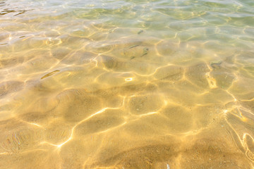 Fototapeta na wymiar Ripples of water waves reflecting texture on a sandy beach bottom