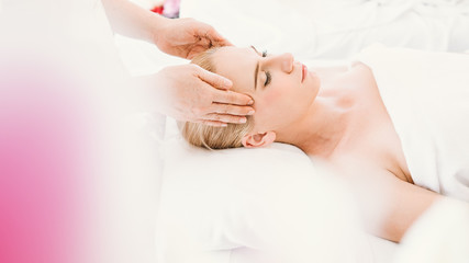 Obraz na płótnie Canvas Beautiful caucasian woman having a facial massage treatment in spa salon with the hands of a therapist as a foreground, selective focus, concept spa and beauty, facial spa treatment, esthetic spa.