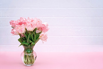 Bouquet of spring fresh flowers of pink tulips in a vase on a white brick wall for Mother's Day, Birthday, Easter, Women's Day. Copy space. Soft selective focus.