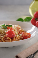Spaghetti in tomato sauce with cherry tomatoes and basil on a white plate on a light background