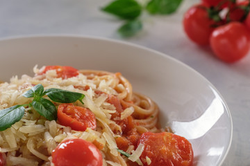 Spaghetti in tomato sauce with cherry tomatoes and basil on a white plate on a light background