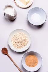 Ingredients for oat porridge: rolled oats or flakes, sugar, salt, milk and butter in a bowls on grey concrete background. Healthy eating, vegetarian food concept. Top view. Selective focus