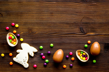 Easter sweets frame. Chocolate eggs and bunny gingerbread on dark wooden background top-down frame copy space
