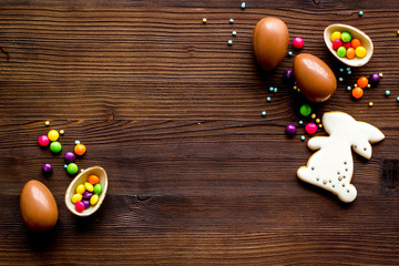 Sweet Easter symbols - chocolate eggs and bunny gingerbread - on dark wooden background top-down frame copy space