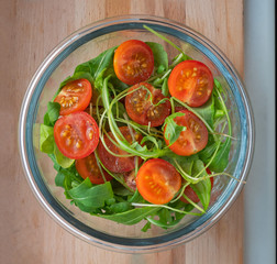 Salad of cherry tomato and fresh arugula in a glass salad bowl on a wooden table