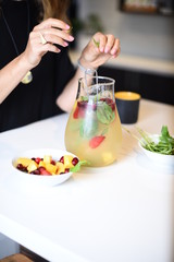 Cold refreshing drink with fruits punch in jug jar with ice and hand morning style interior 