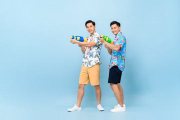Smilng happy male friends playing with water guns in blue isolated background for Songkran festival in Thailand and southeast Asia