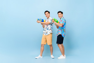 Fototapeta premium Smilng happy male friends playing with water guns in blue isolated background for Songkran festival in Thailand and southeast Asia