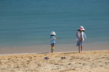初夏の海の砂浜で遊んでいる子供姉妹