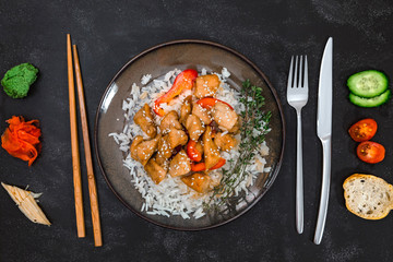 Tasty chicken with rice on brown plate on black background. Asian vs European cuisines. friendship and comparison.