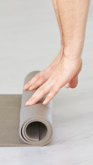 Yoga person rolling sport mat. Grey color. Gym carpet. Arms roll pad. Closeup concept with copyspace. Aerobics matt. Fitness club floor. Male nands. Teacher class background