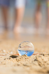 初夏の海の砂浜で遊んでいる子供姉妹と透明な水晶ガラスボール