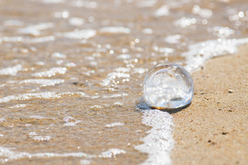 夏の海の砂浜にある透明な水晶ガラスボール