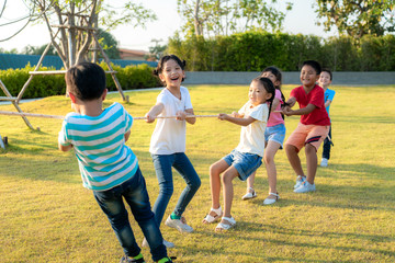 Group of happy young Asian children playing tug of war or pull rope togerther outside in city park playground in summer day. Children and recreation concept..